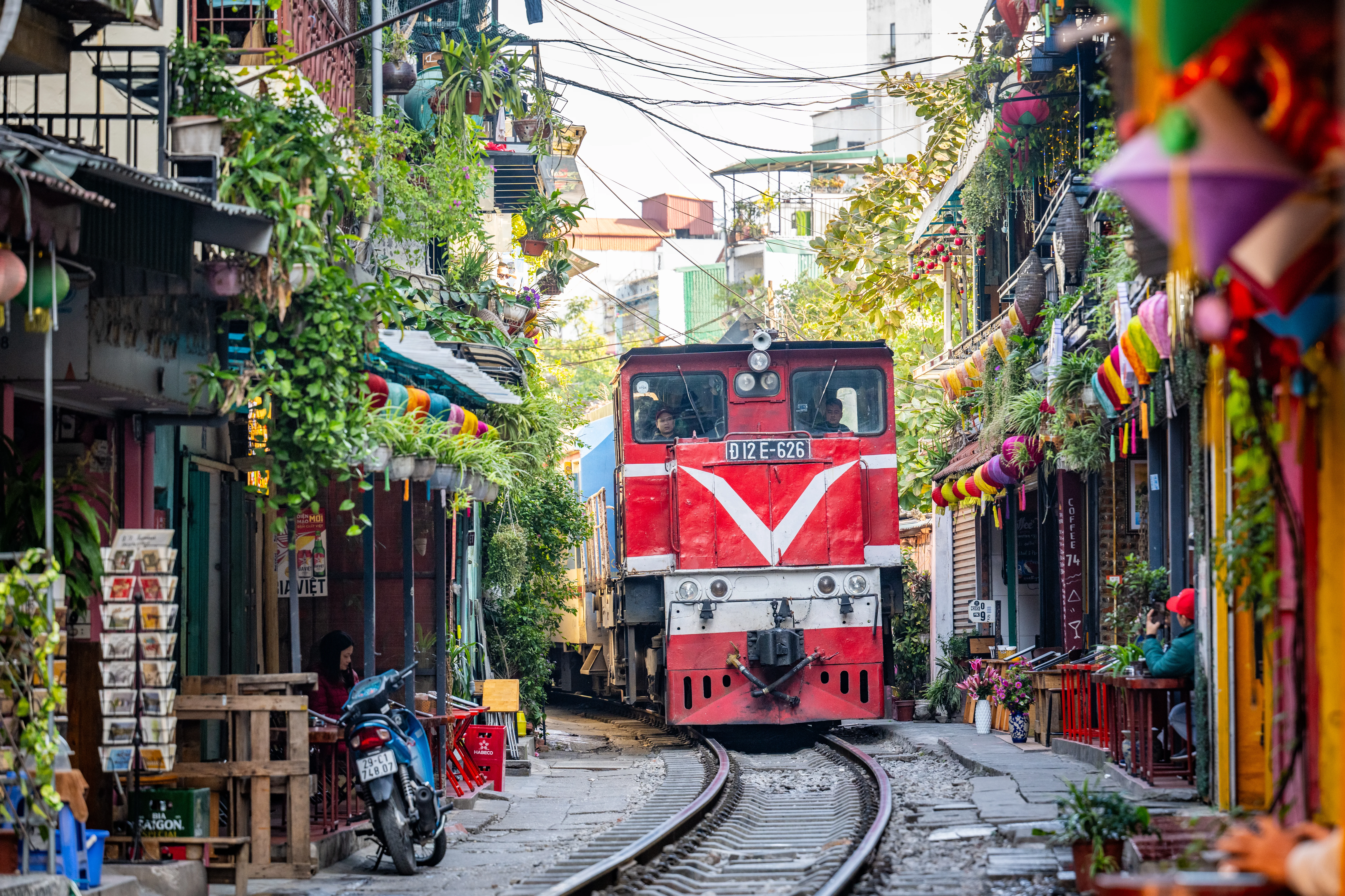 Express train passing through narrow Hanoi Train Street alley lined with balcony cafes